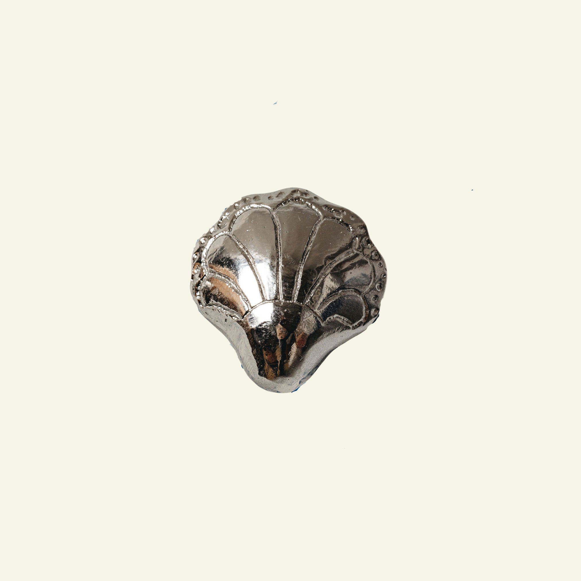 Silver shell-shaped object on a beige background
