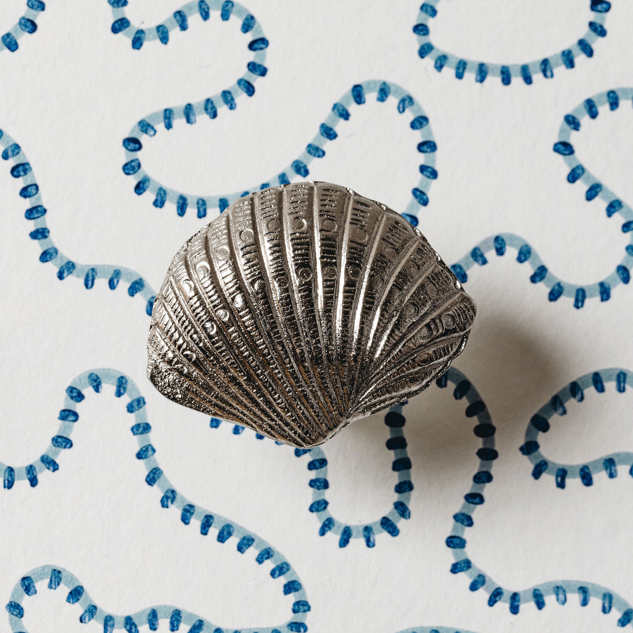 Silver shell-shaped object on a white background with blue decorative elements