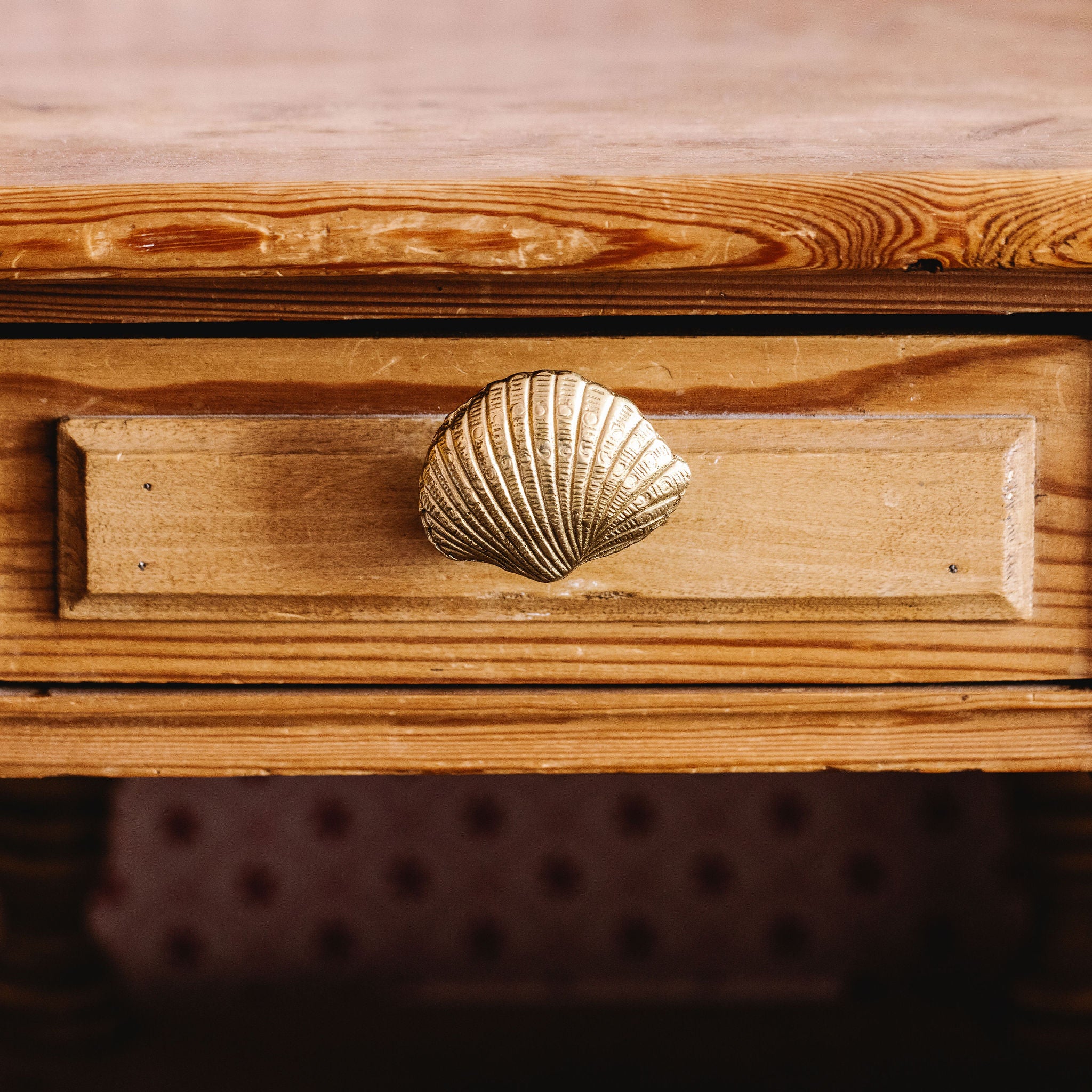 Wooden drawer with a shell-shaped brass handle on a wooden surface.