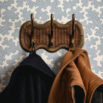 Wicker coat rack with two jackets against a patterned wall.
