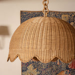 Wicker lampshade hanging against a decorative wall with floral patterns.