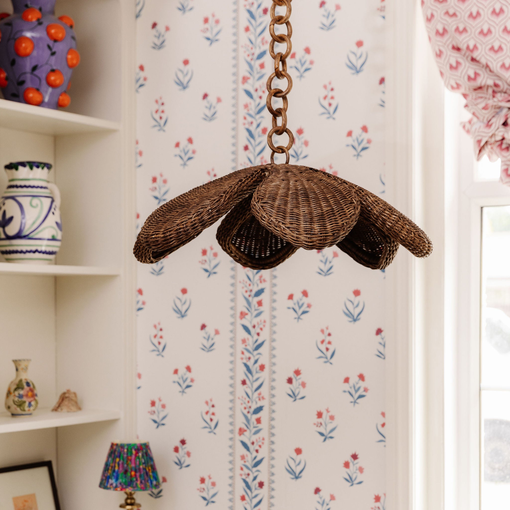 Floral wicker ceiling light fixture hanging in a room with floral wallpaper and decorative vases.