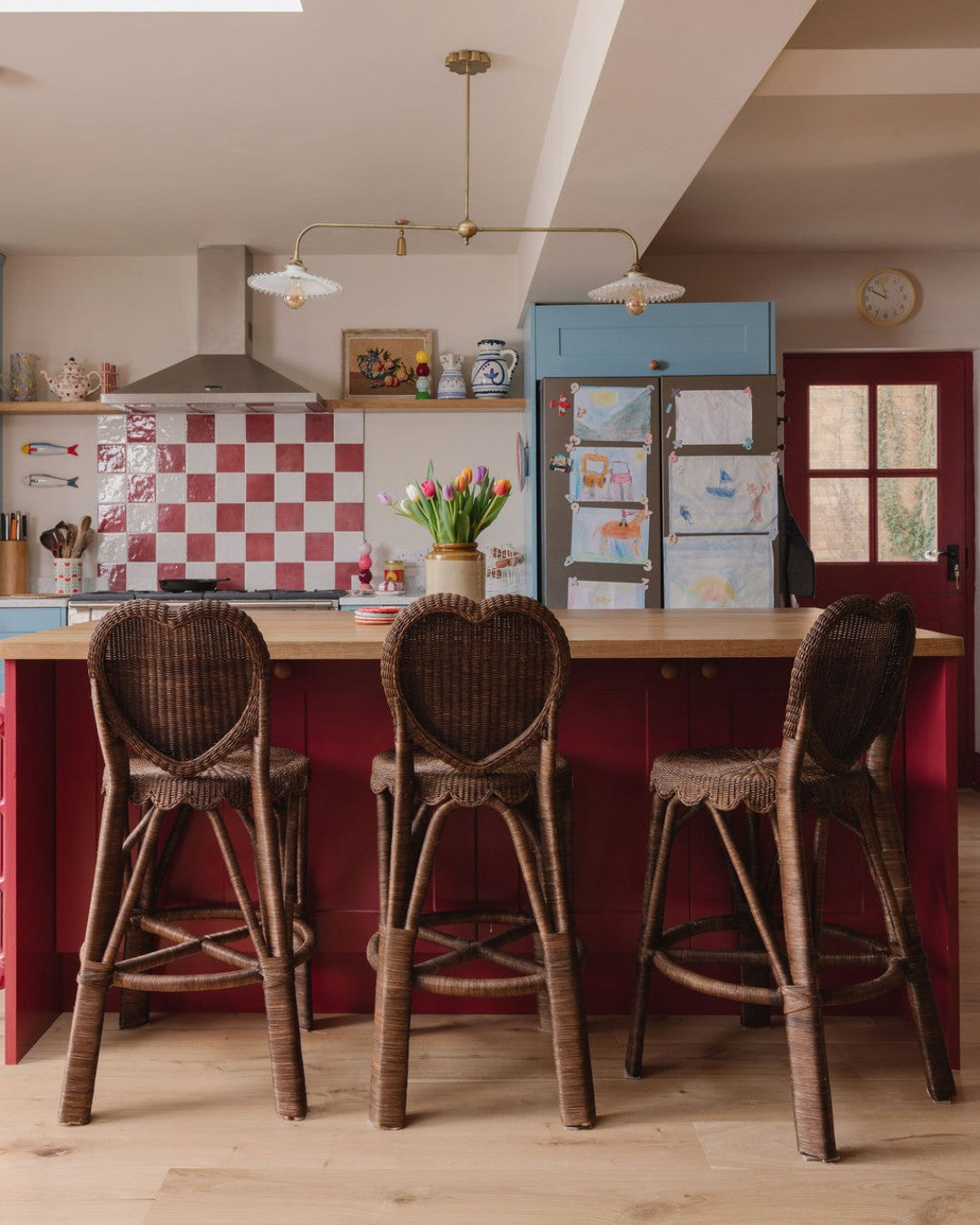 Kitchen with wooden island and wicker bar stools, checkered backsplash, and colorful refrigerator.