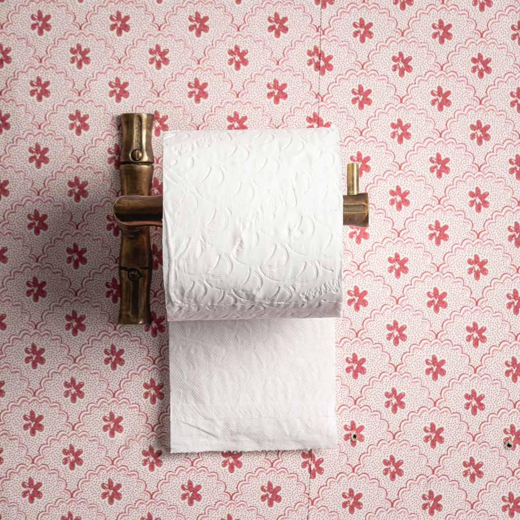 Roll of white paper towels on a brass holder against a pink floral wallpaper background