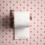 Roll of white paper towels on a brass holder against a pink floral wallpaper background