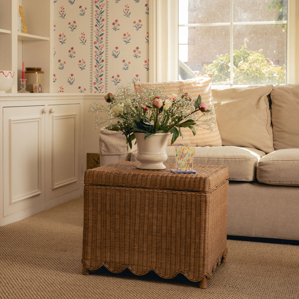 Living room with a wicker ottoman, floral arrangement, and beige sofa.