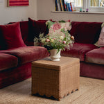 Red velvet sofa with a floral arrangement on a woven ottoman in a cozy living room.