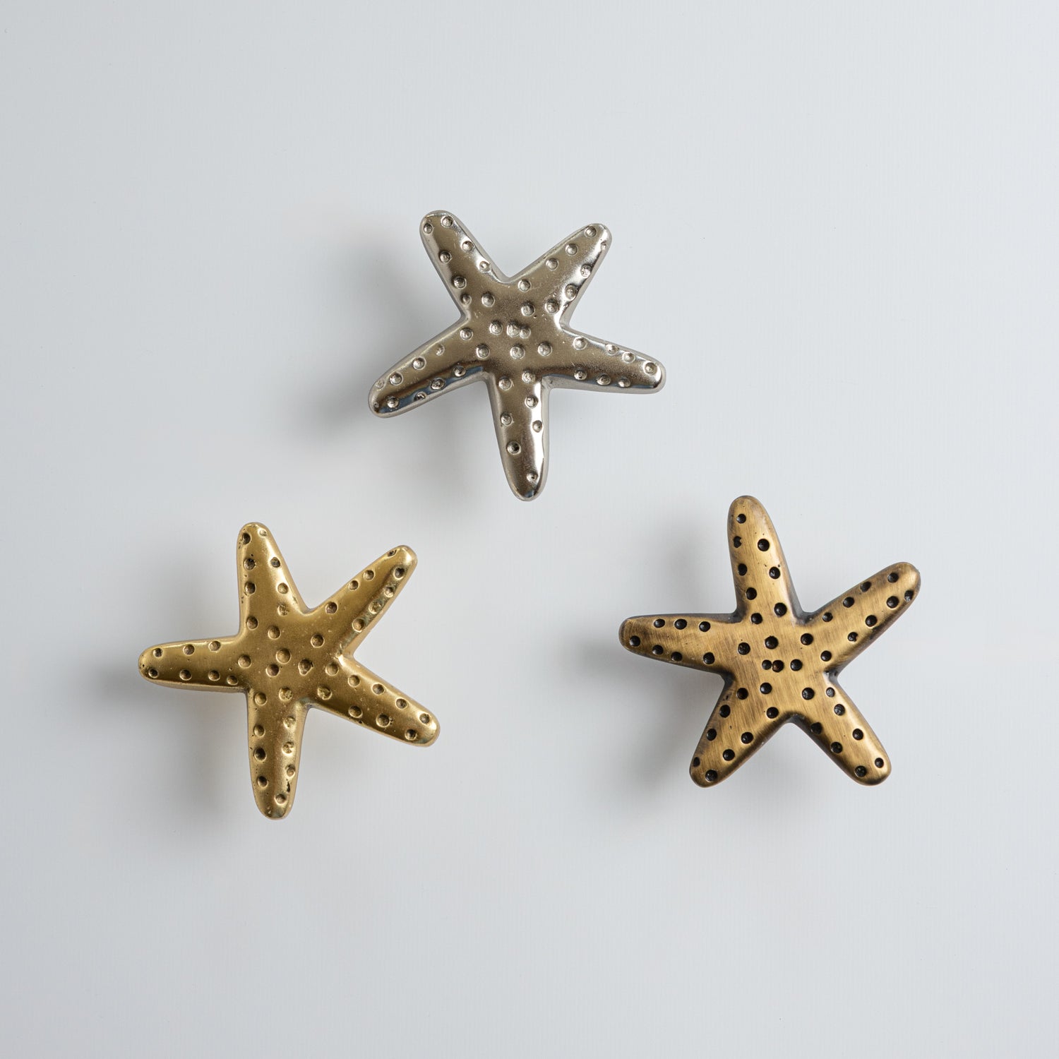Three starfish-shaped knobs, one gold and one silver, on a light gray background.